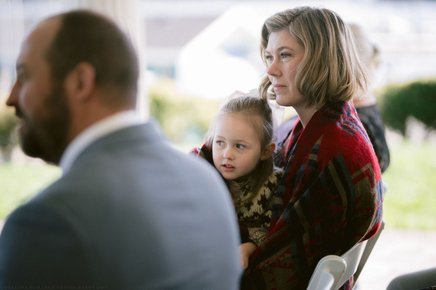 Woman holding young child at outdoor wedding ceremony seating.