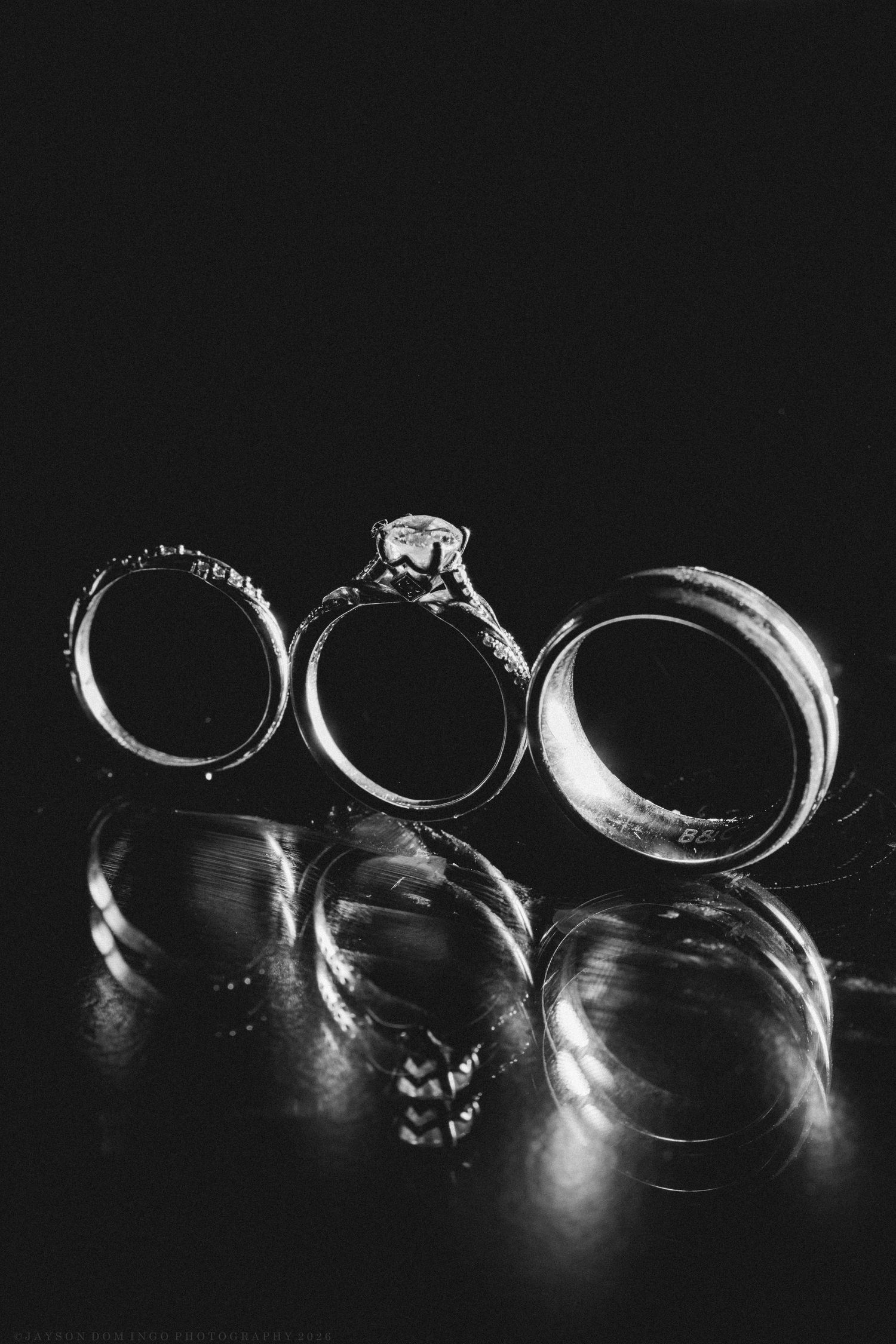 Three wedding rings displayed upright on a reflective black surface in elegant black and white photography.