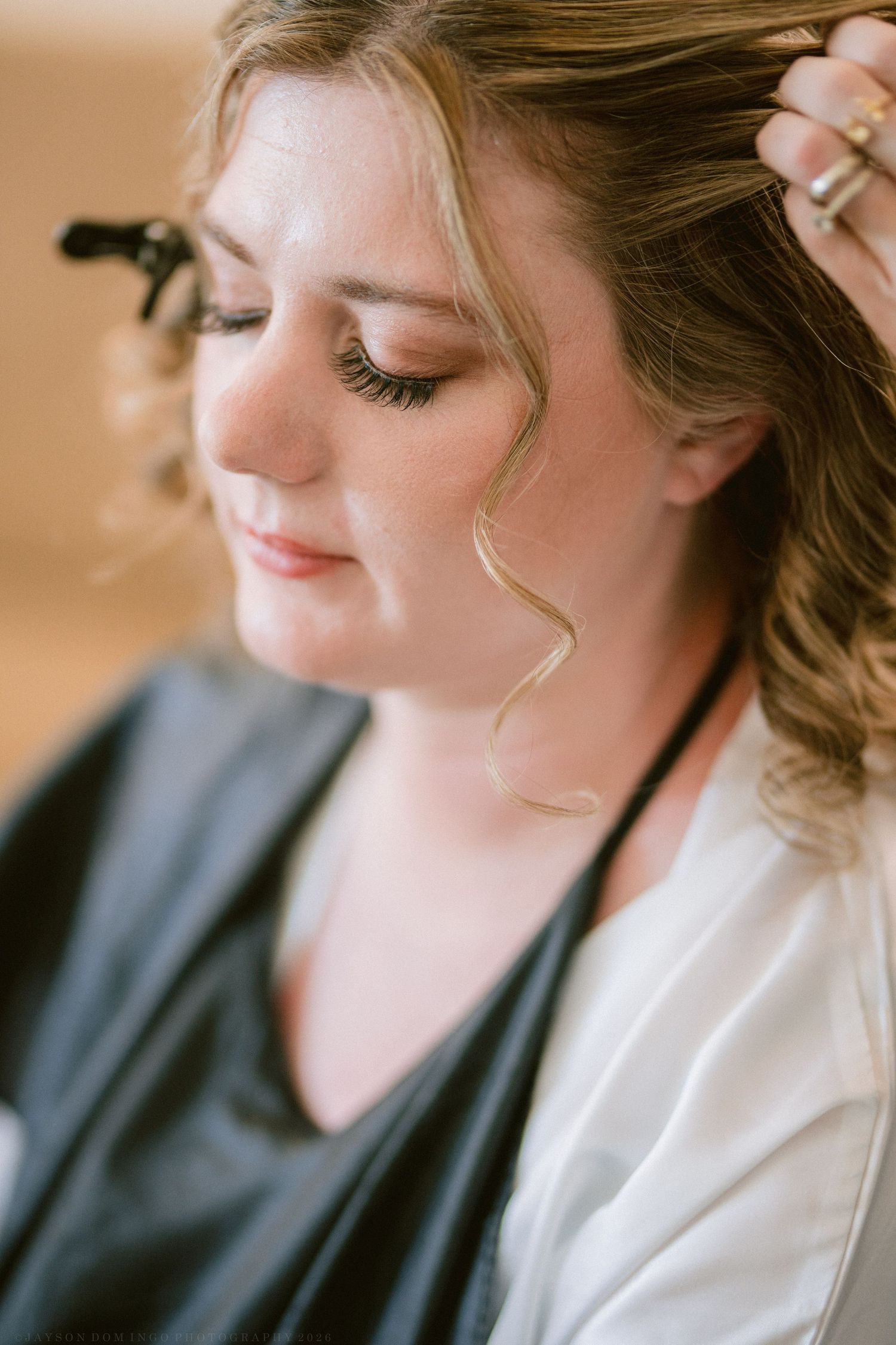 Close-up of a bride with curled hair and elegant makeup wearing a gold earring during wedding prep.