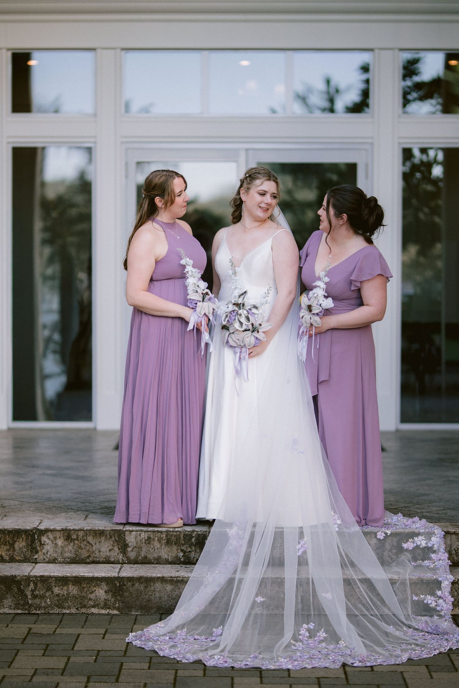 Bride with two bridesmaids in purple dresses holding floral bouquets.