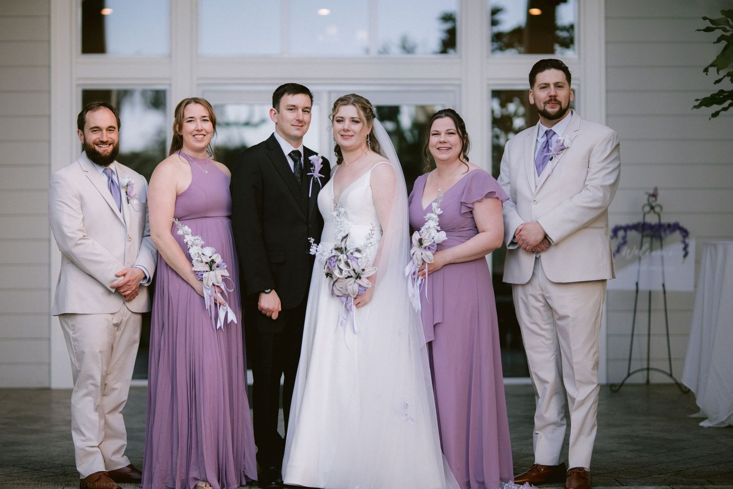 Wedding party poses in lavender bridesmaid dresses and tan suits with bride and groom.