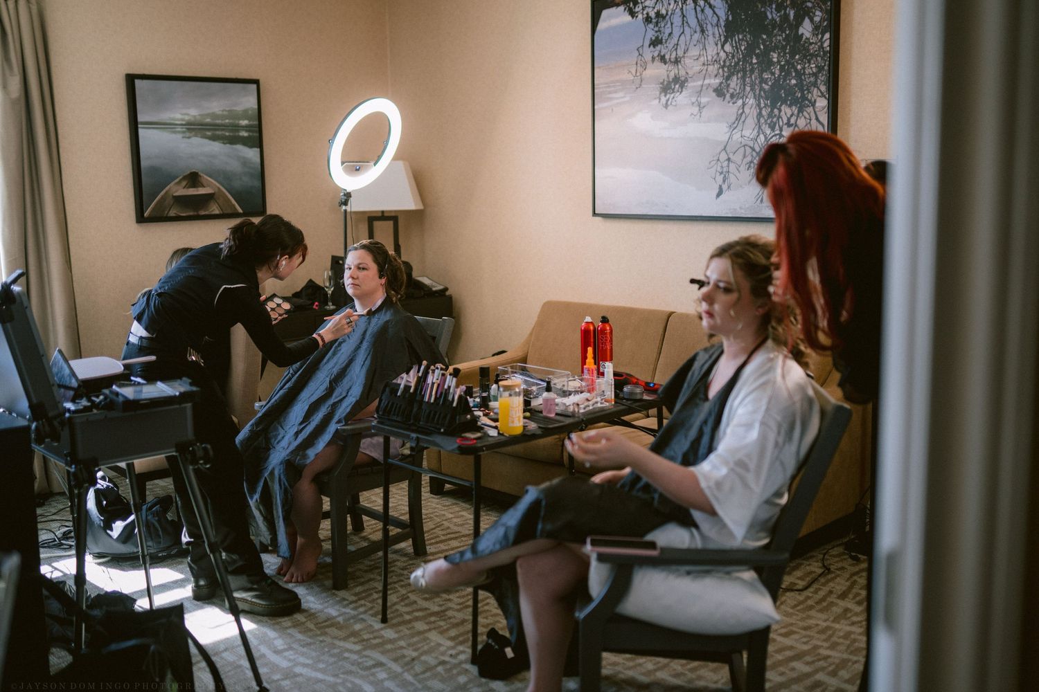 Bridal party getting hair and makeup done in a hotel room with ring lights and styling tools.