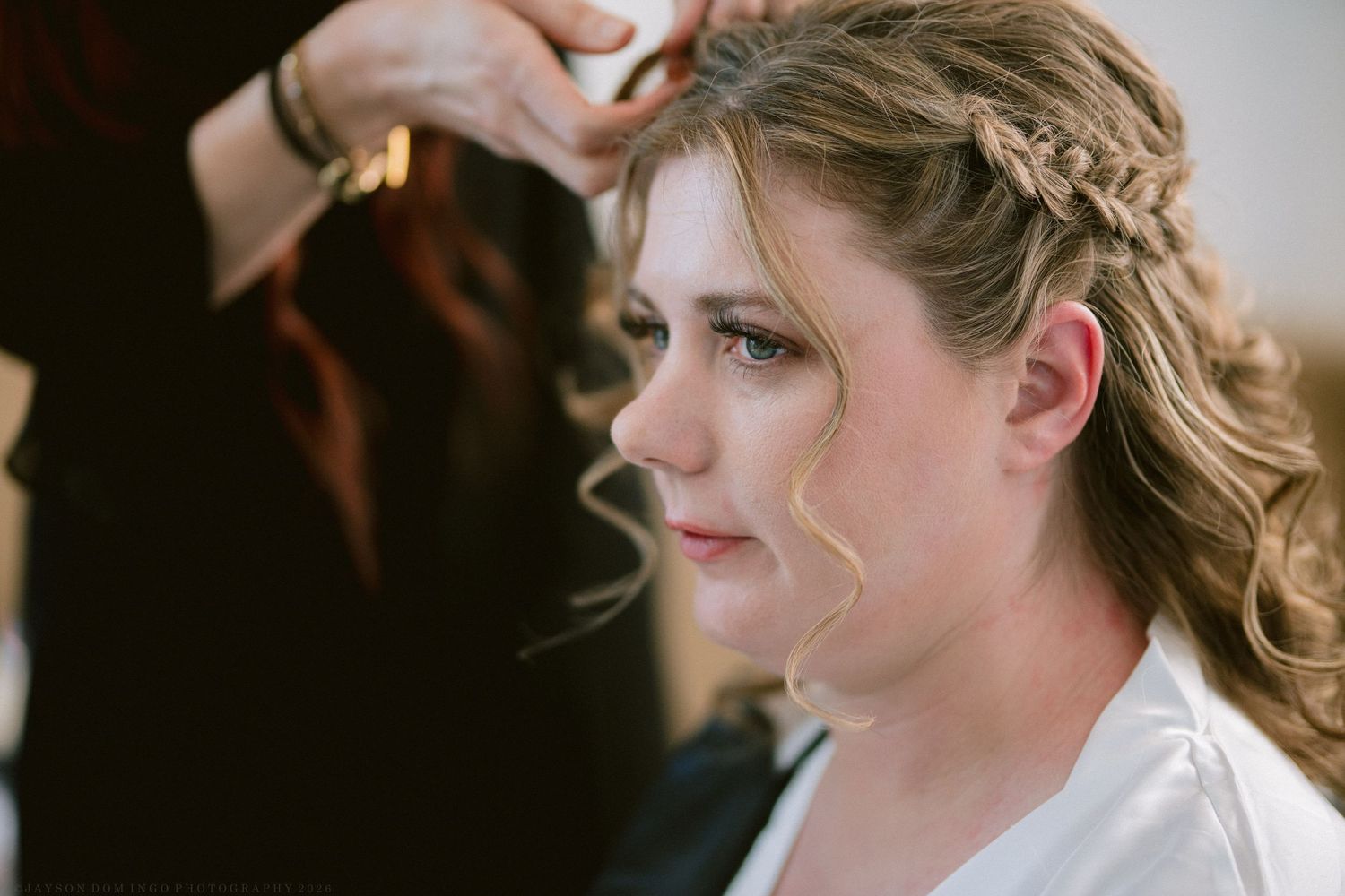 Bride getting her braided updo hairstyle done by a stylist on her wedding day.