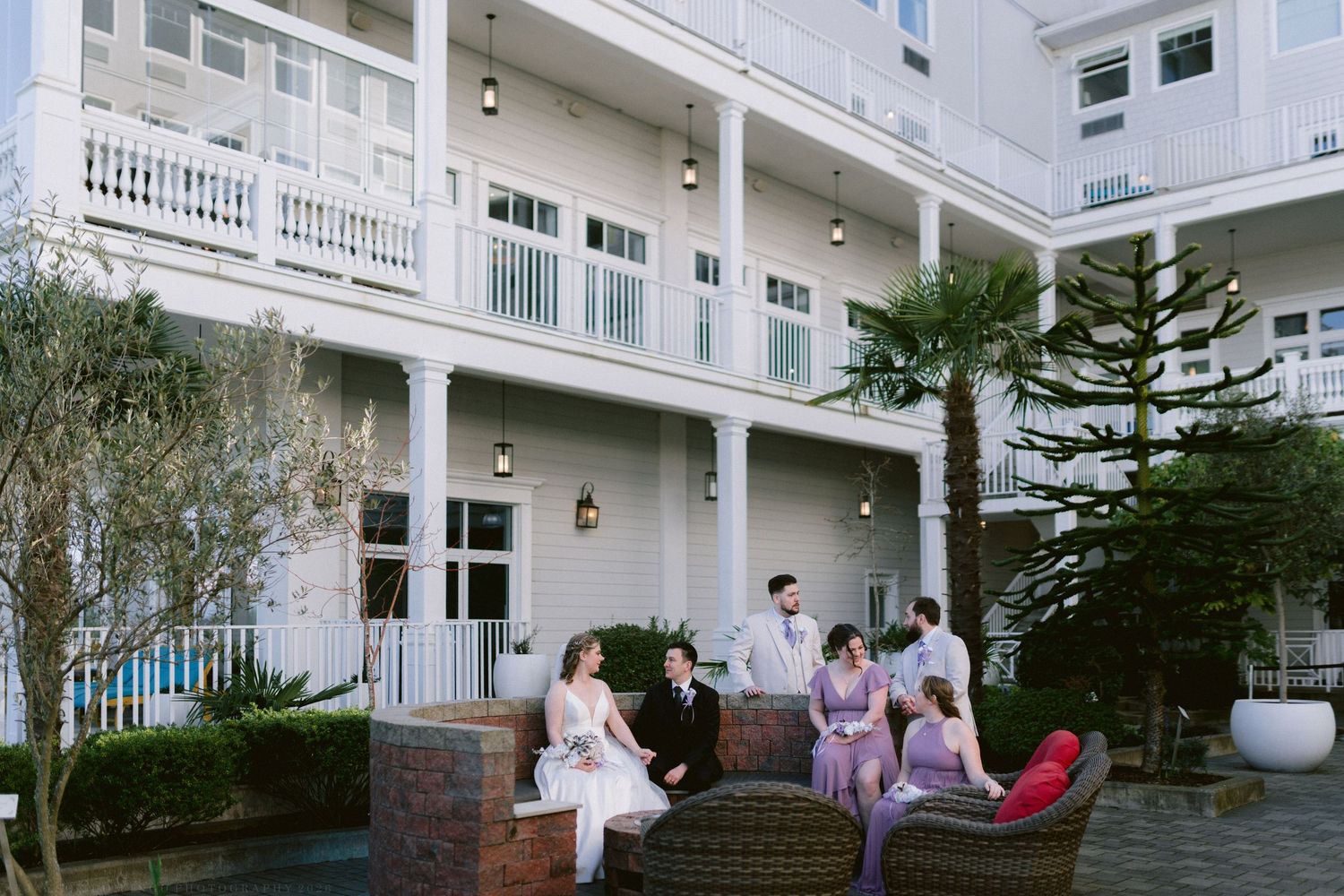 Wedding party gathered on elegant hotel courtyard patio with palm trees.