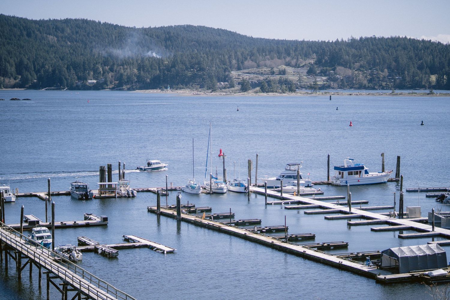 Aerial view of a scenic marina with boats docked at wooden piers on a calm lake surrounded by forested hills.