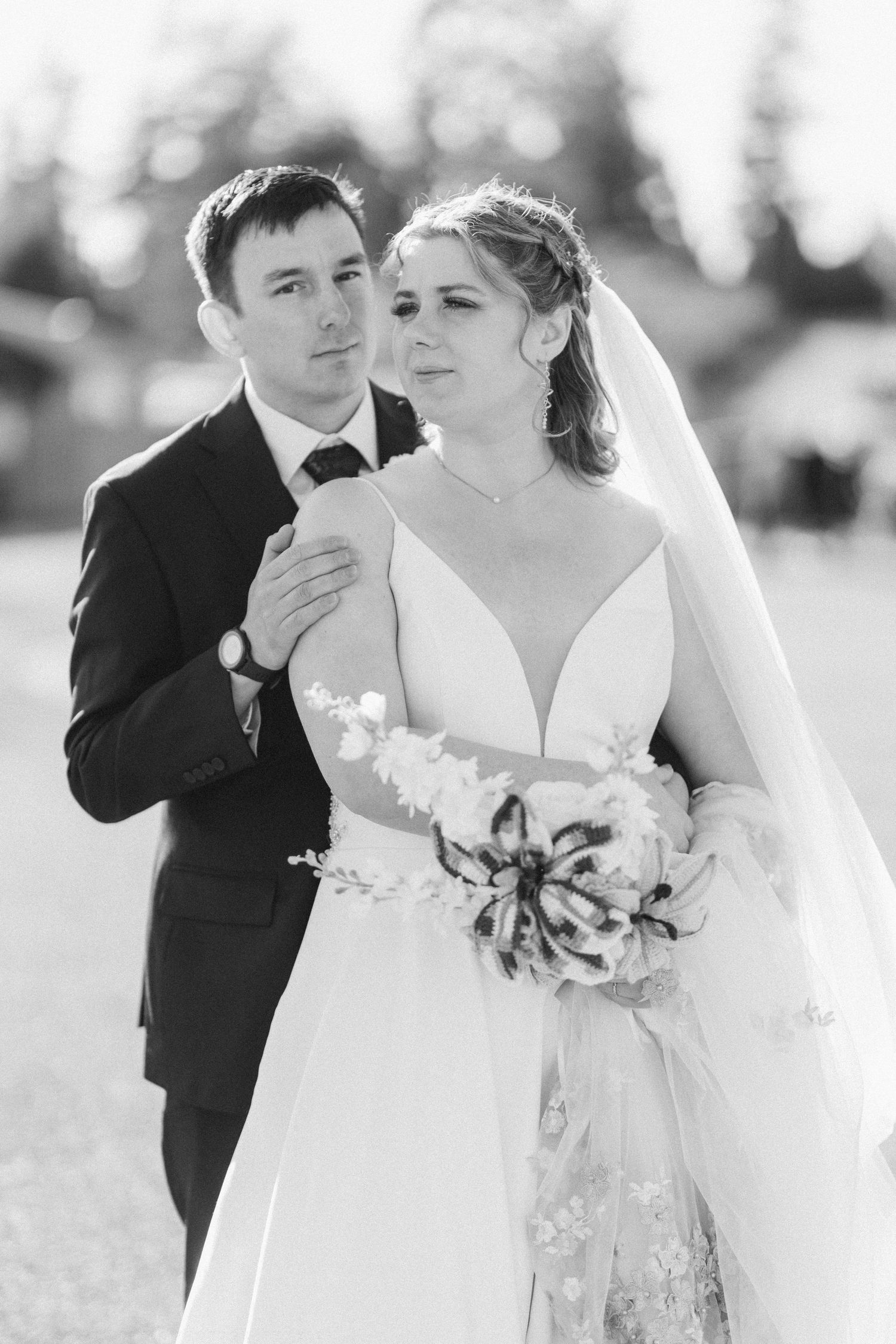 A bride and groom share a tender moment outdoors in classic black and white wedding portrait.