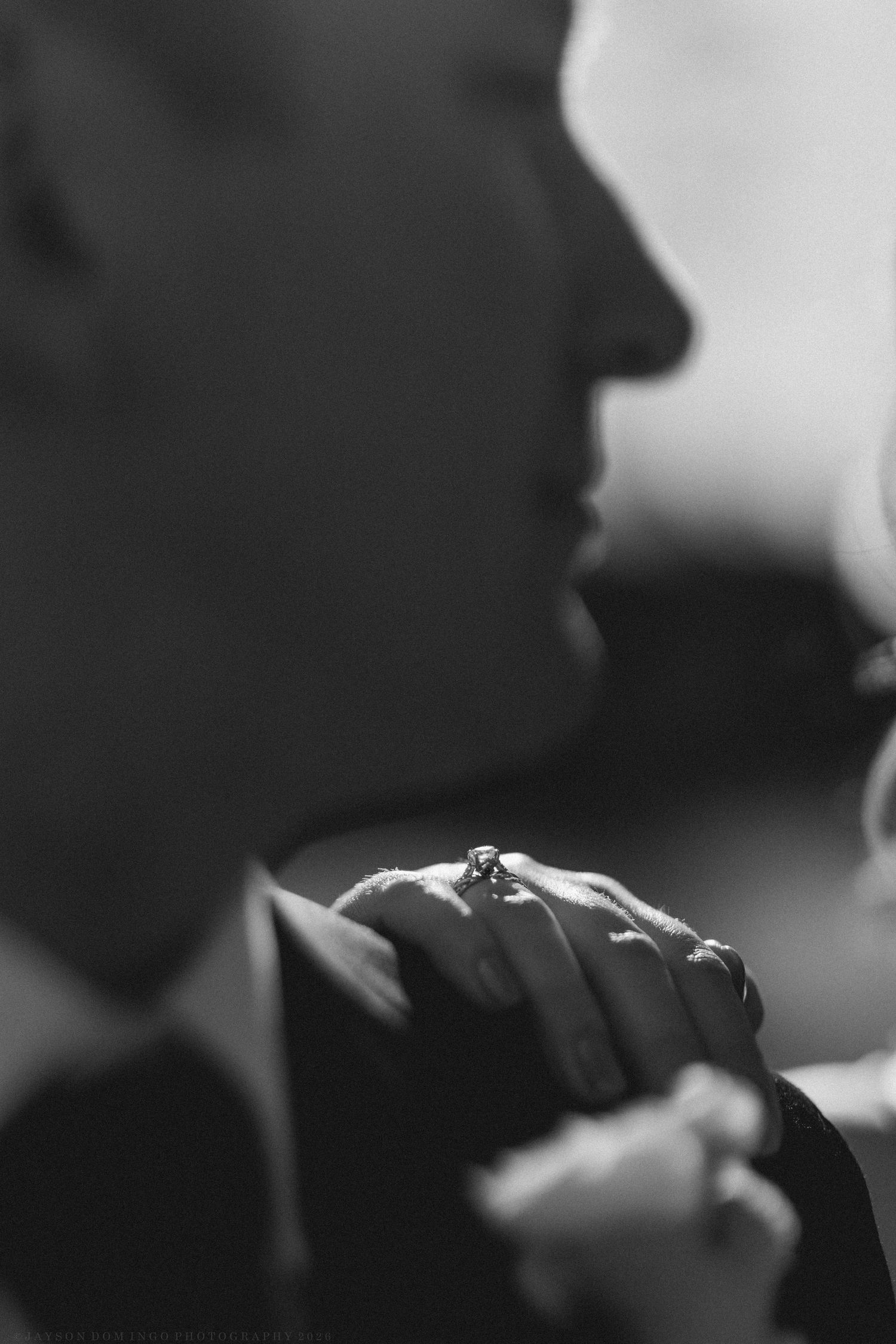 Black and white close-up of bride and groom holding hands, showcasing a diamond engagement ring.