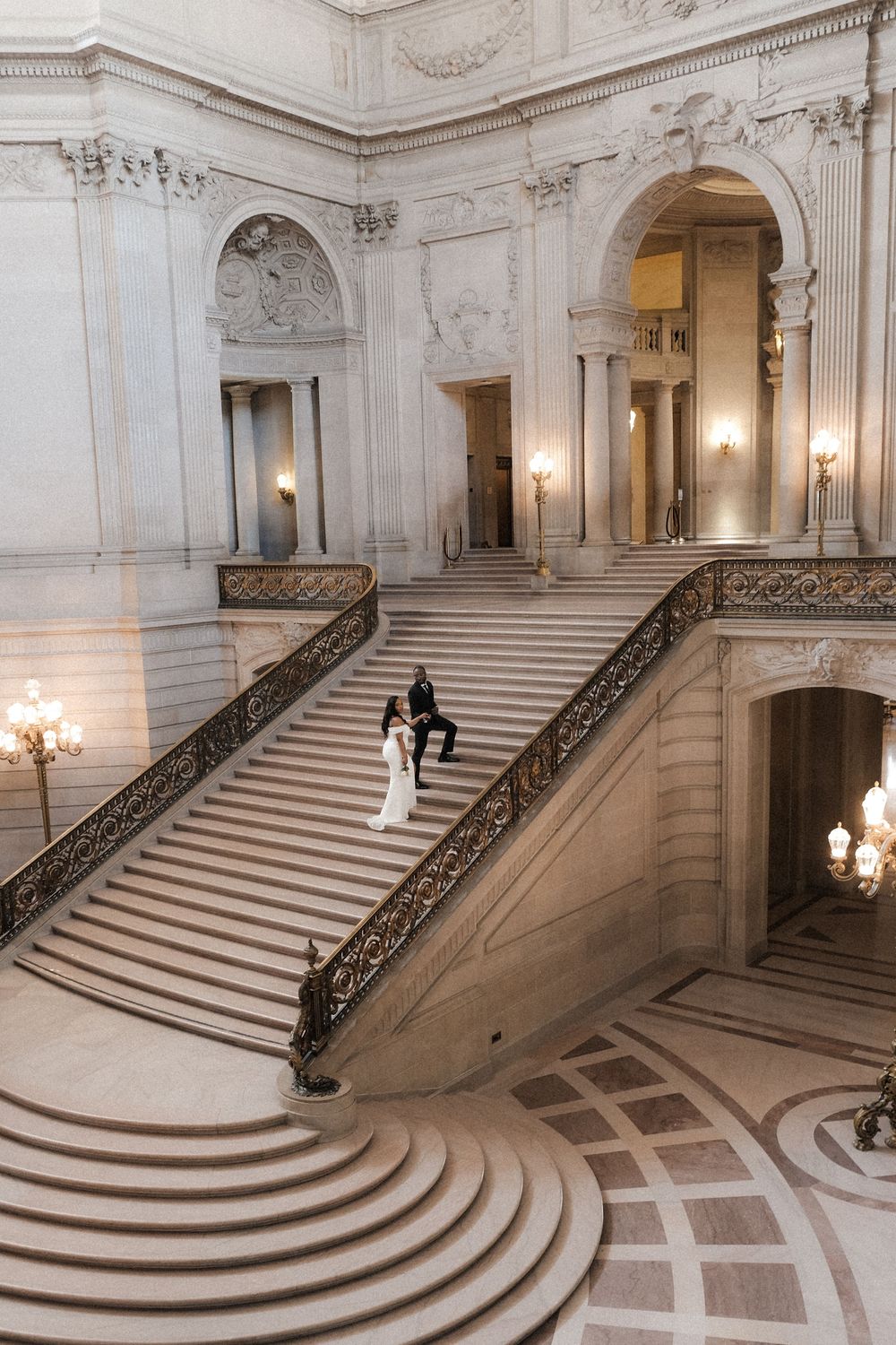 Bride and groom pose on grand marble staircase at San Francisco City Hall during elegant wedding ceremony.