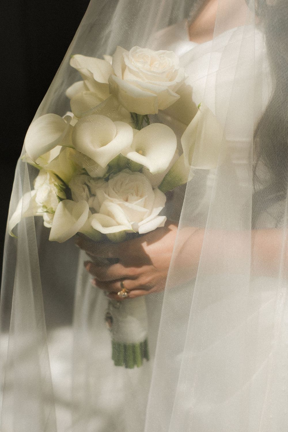 Bride holding a white wedding bouquet of roses and calla lilies, draped in a flowing veil.