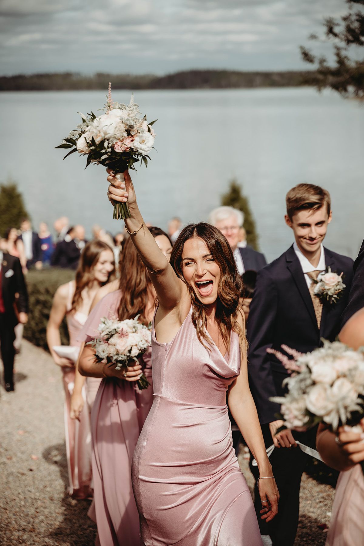 Brudtärna håller upp sin bukett i luften och skriker av glädje under vigsel på Rockelstad slott i Sörmland, fotograf Lets Bloom Media.