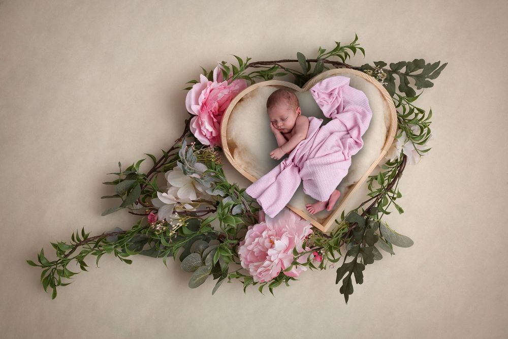 Creative newborn photography with heart-shaped floral frame and pink accents.