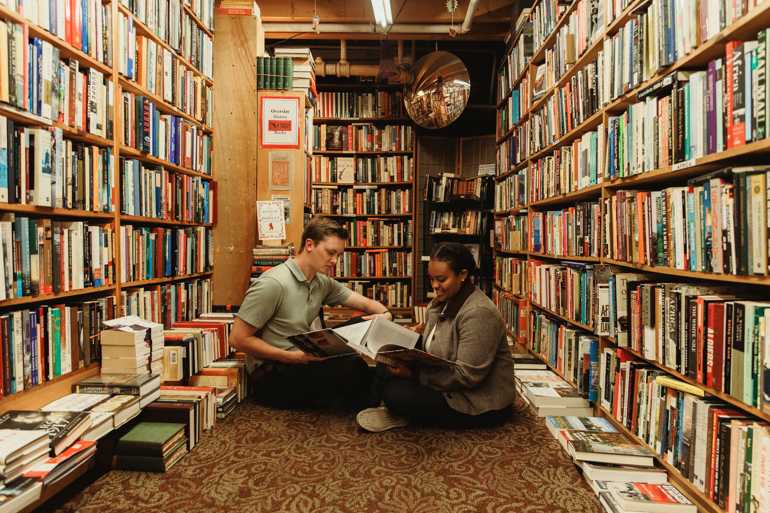 Long rows of bookshelves filled with used books stretch down a narrow aisle in a cozy bookstore.