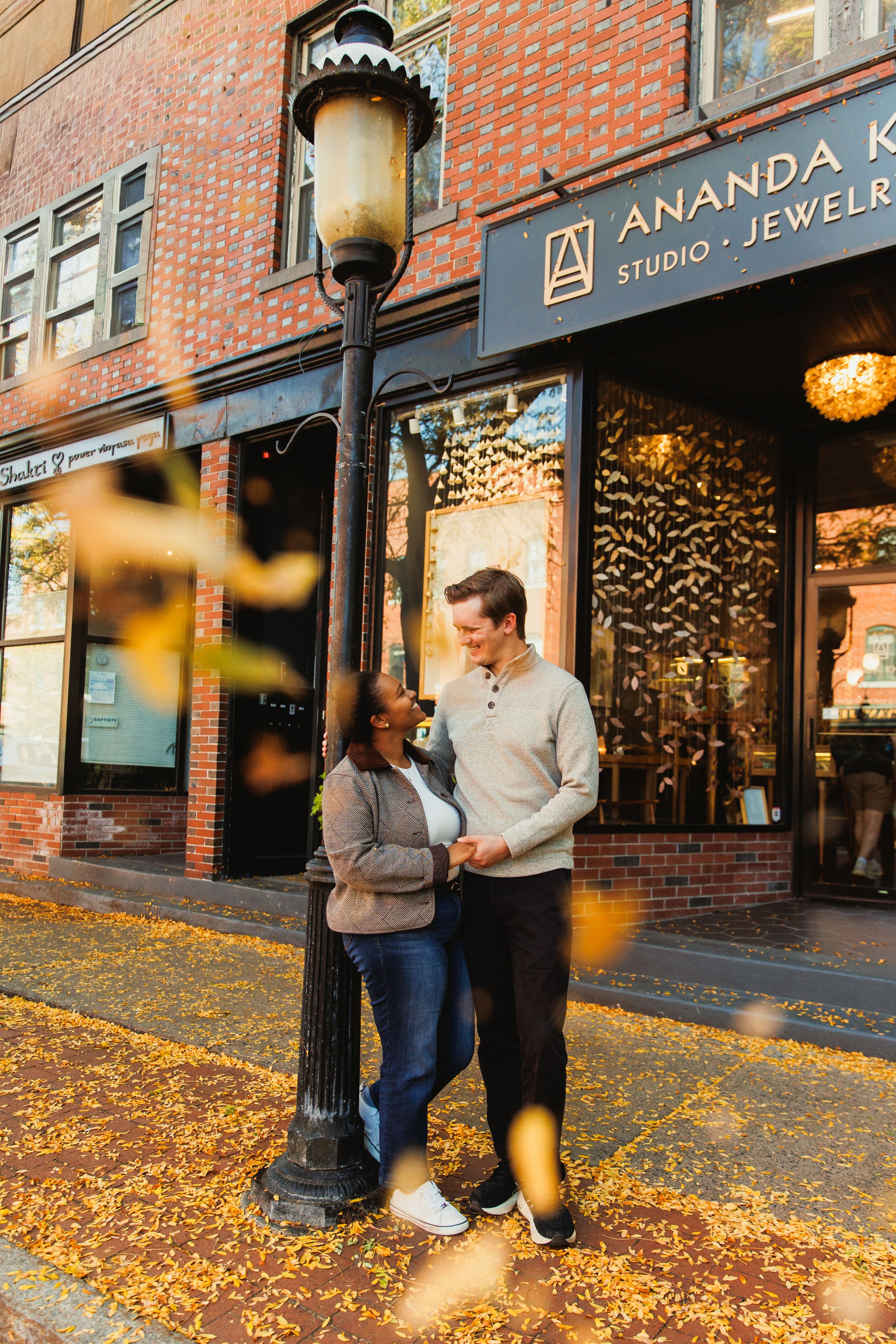 A couple standing by a vintage lamppost outside Ananda Jewelers with fall leaves scattered on the ground.