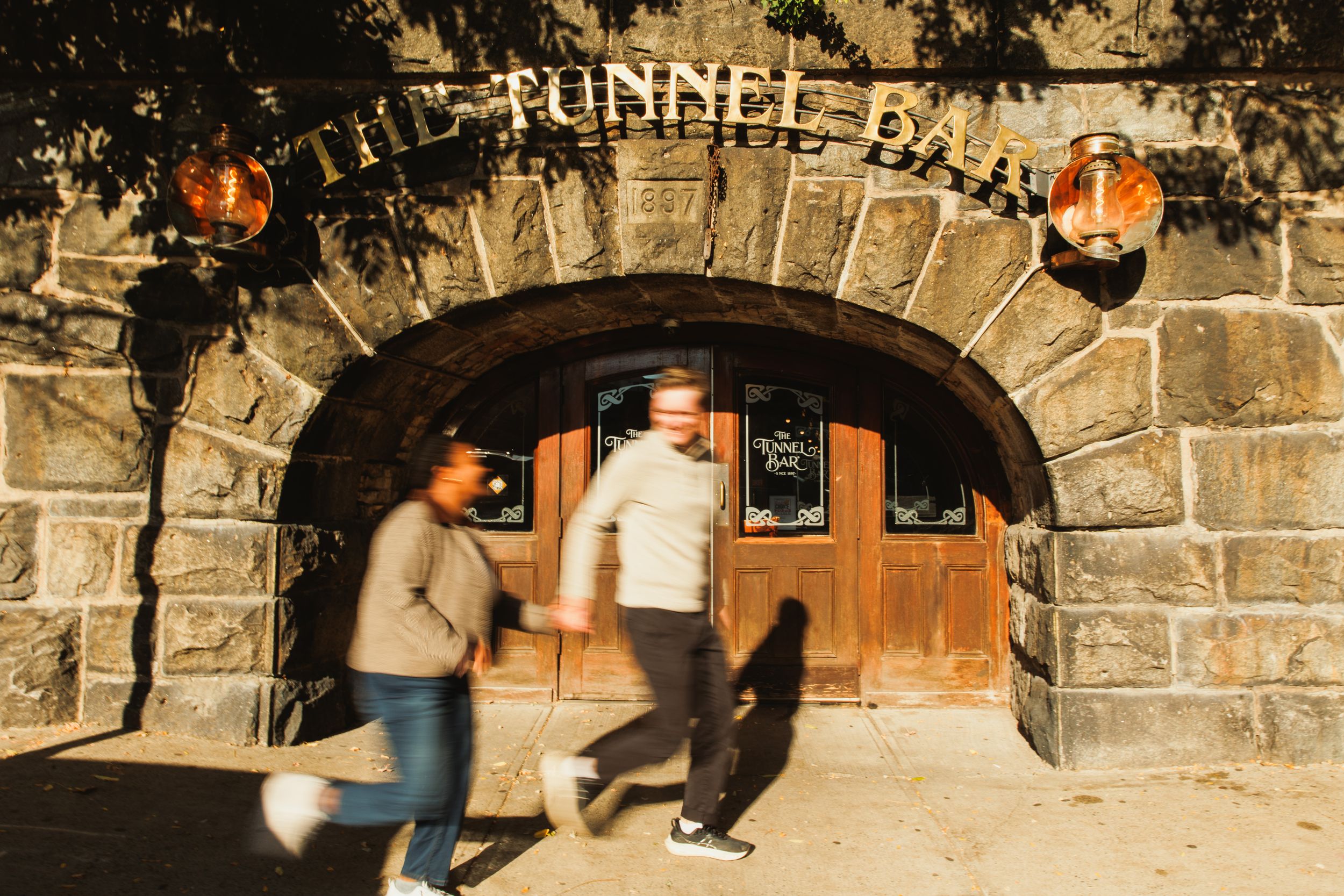 A series of stone archways in a tunnel with people walking through and warm lighting illuminating the path.