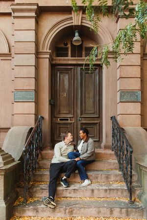 Series of brownstone steps and doorways with ornate iron railings on a fall day with scattered leaves.