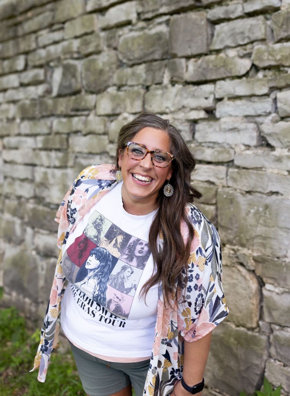 A person wearing glasses and a white t-shirt poses cheerfully against a rustic stone wall.