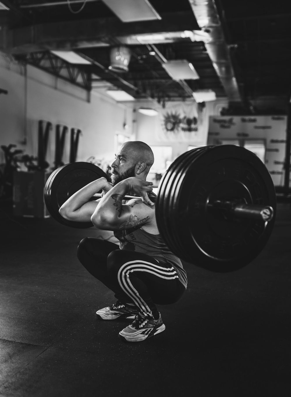 Athlete performs heavy front squat with barbell in dark gym setting captured in black and white photography.