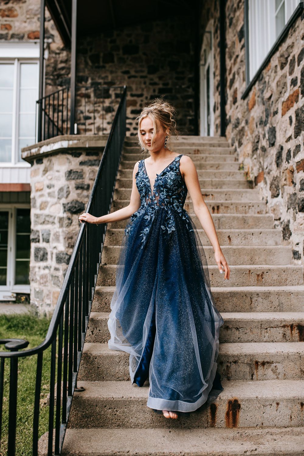 Flowing navy blue gown with detailed bodice on stone staircase with wrought iron railing.