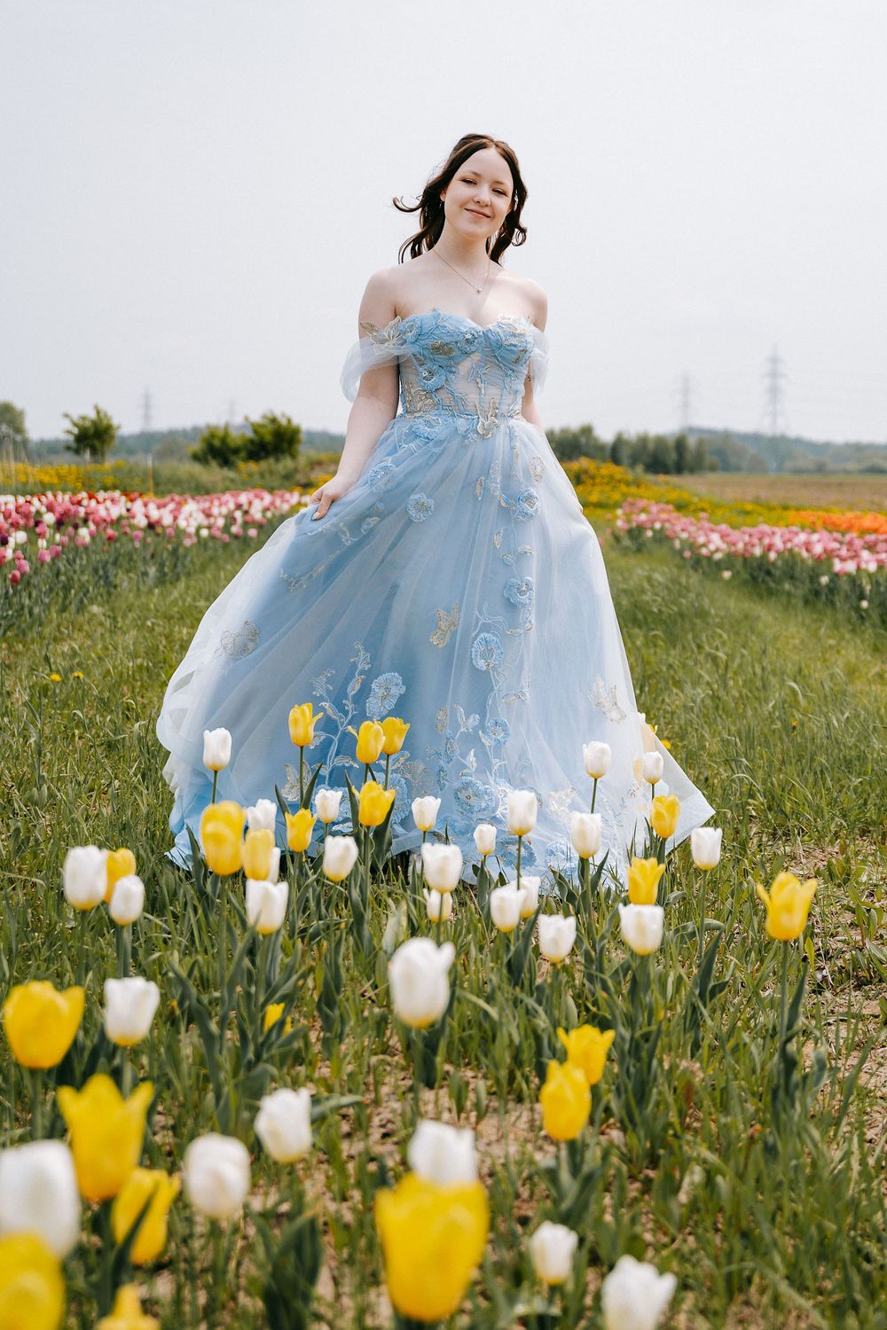 A flowing powder blue gown twirls gracefully amidst a field of blooming yellow and white tulips.