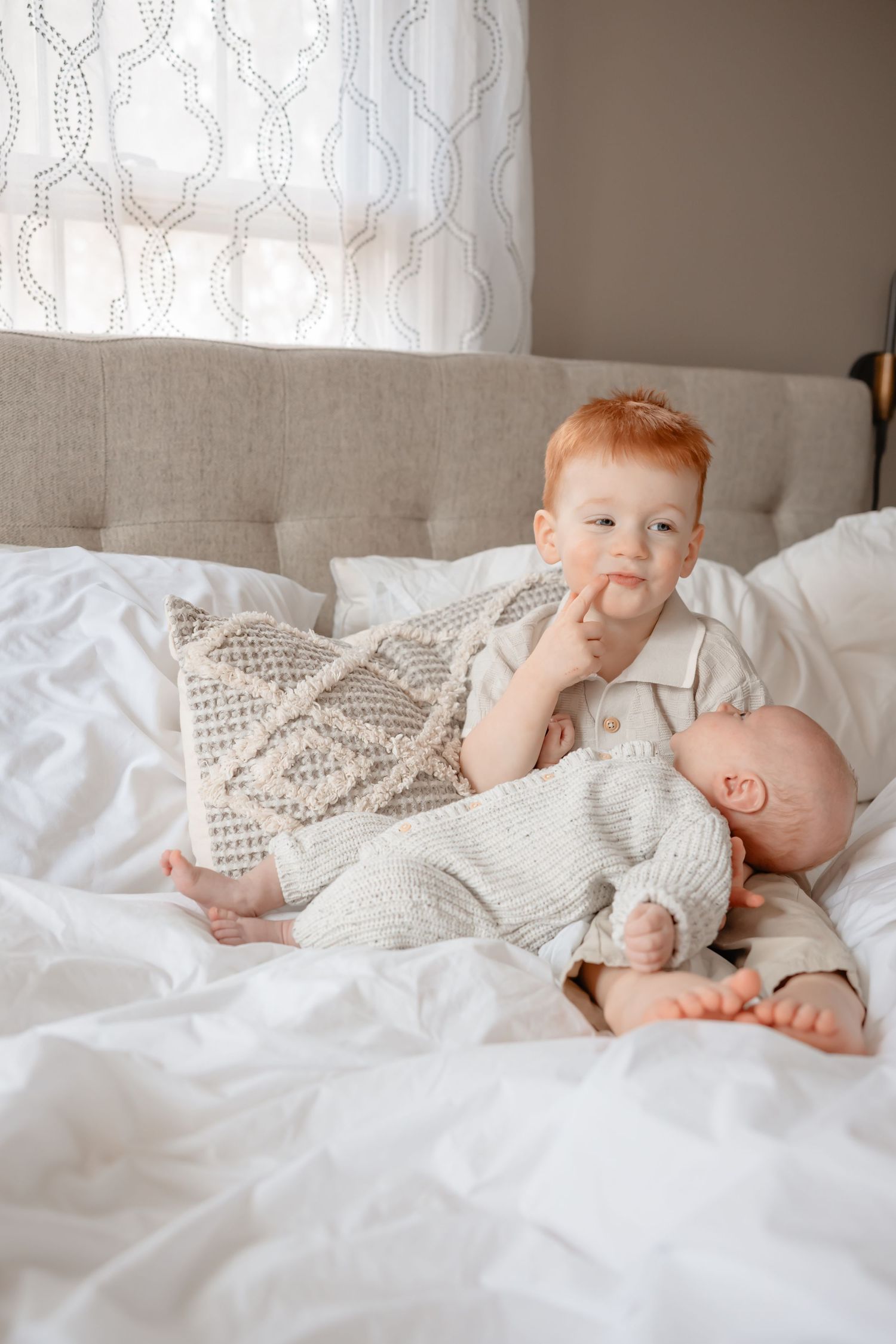 A baby in a white knit sweater lies on white bedding in a series of connected photos showing different poses.