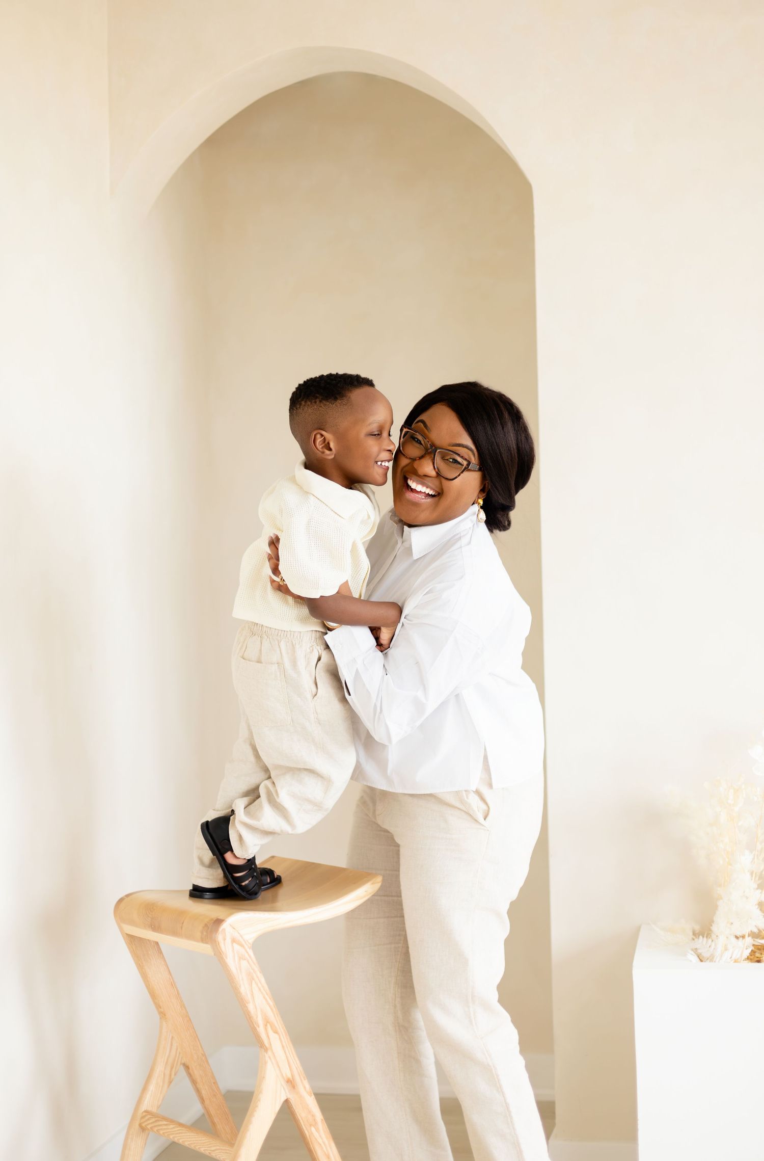 A heartwarming parent-child moment captured in white outfits against a neutral backdrop in a minimalist setting.