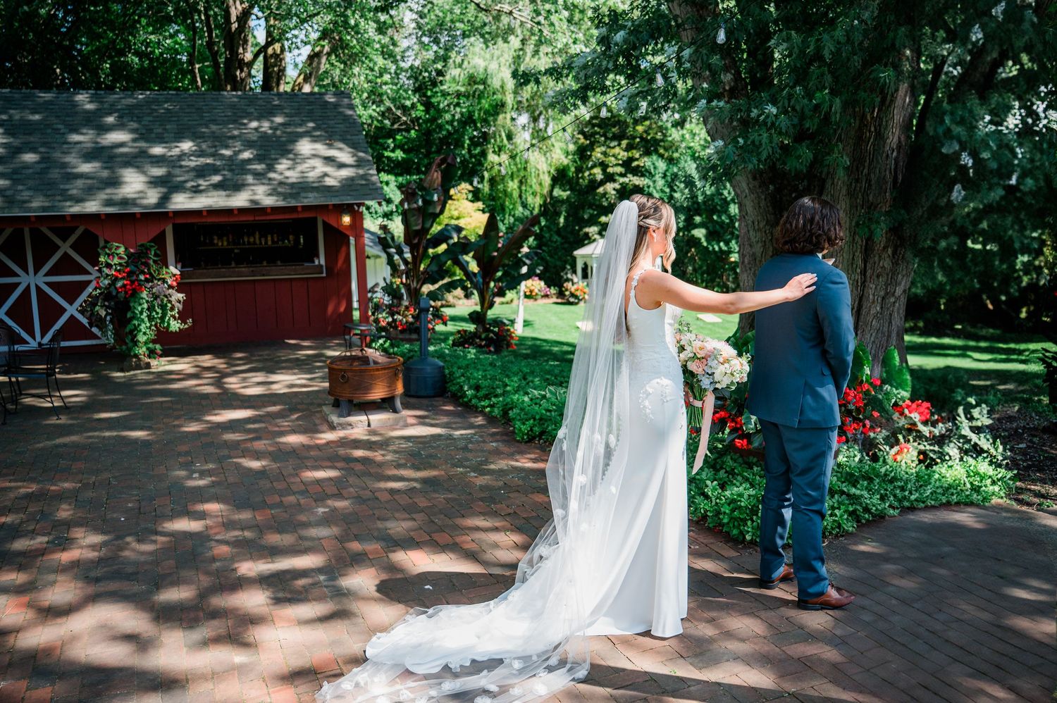 A couple shares a romantic dance moment on a wooden deck surrounded by lush greenery and a red barn in the background.