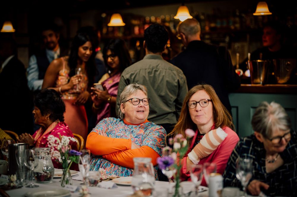 People gathered around tables at a dimly lit event venue with orange and pink ambient lighting.