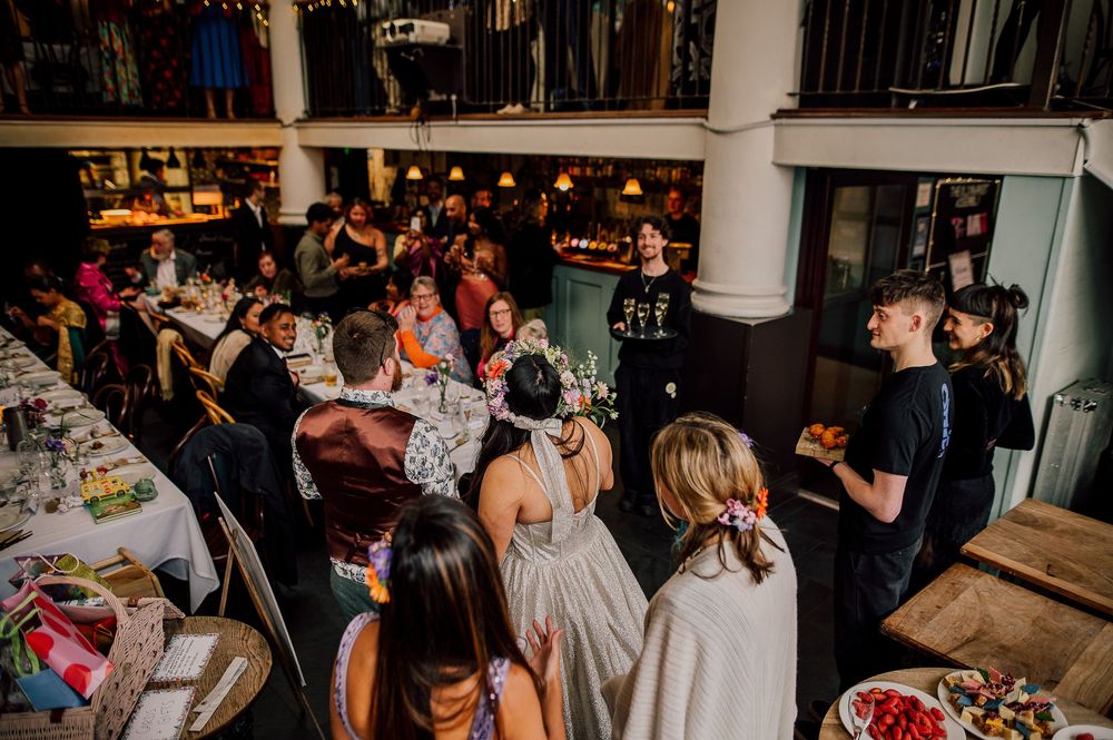 A crowded wedding reception venue with guests mingling and dancing on the dance floor in a dimly lit room.