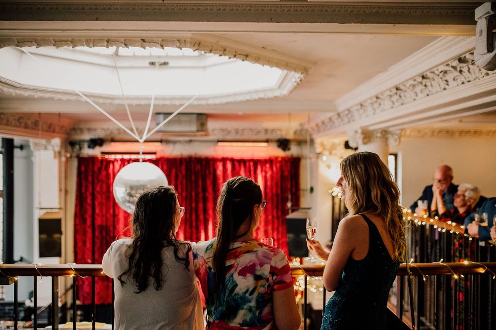 Elegant ballroom interior with ornate crown molding, red curtains, and chandeliers casting warm lighting.