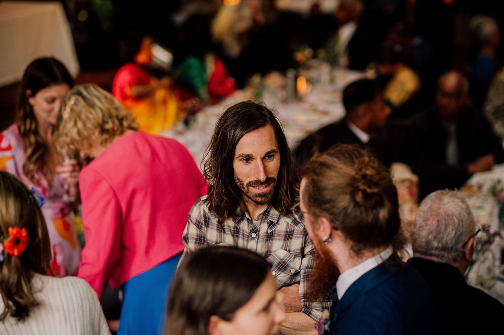 People gather at a social event in a dimly lit indoor setting with tables and guests mingling in conversation.