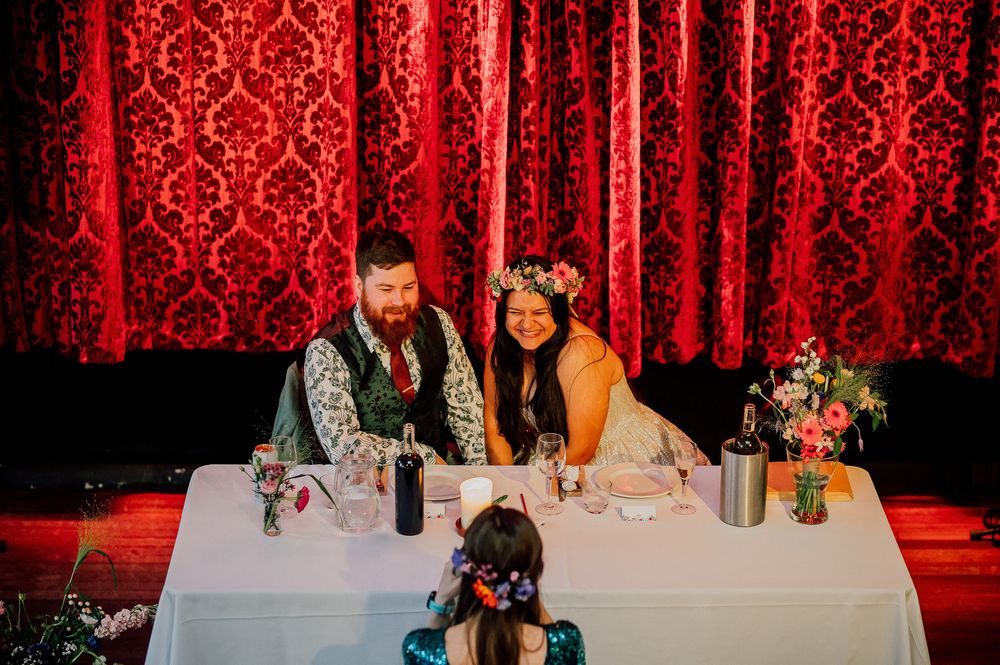 Wedding reception tables decorated with elegant floral centerpieces against a dramatic red damask backdrop.