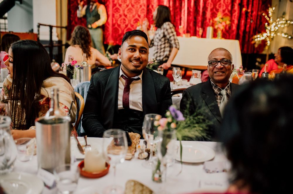 Wedding guests enjoying dinner at elegantly decorated reception tables with red decor and floral centerpieces.