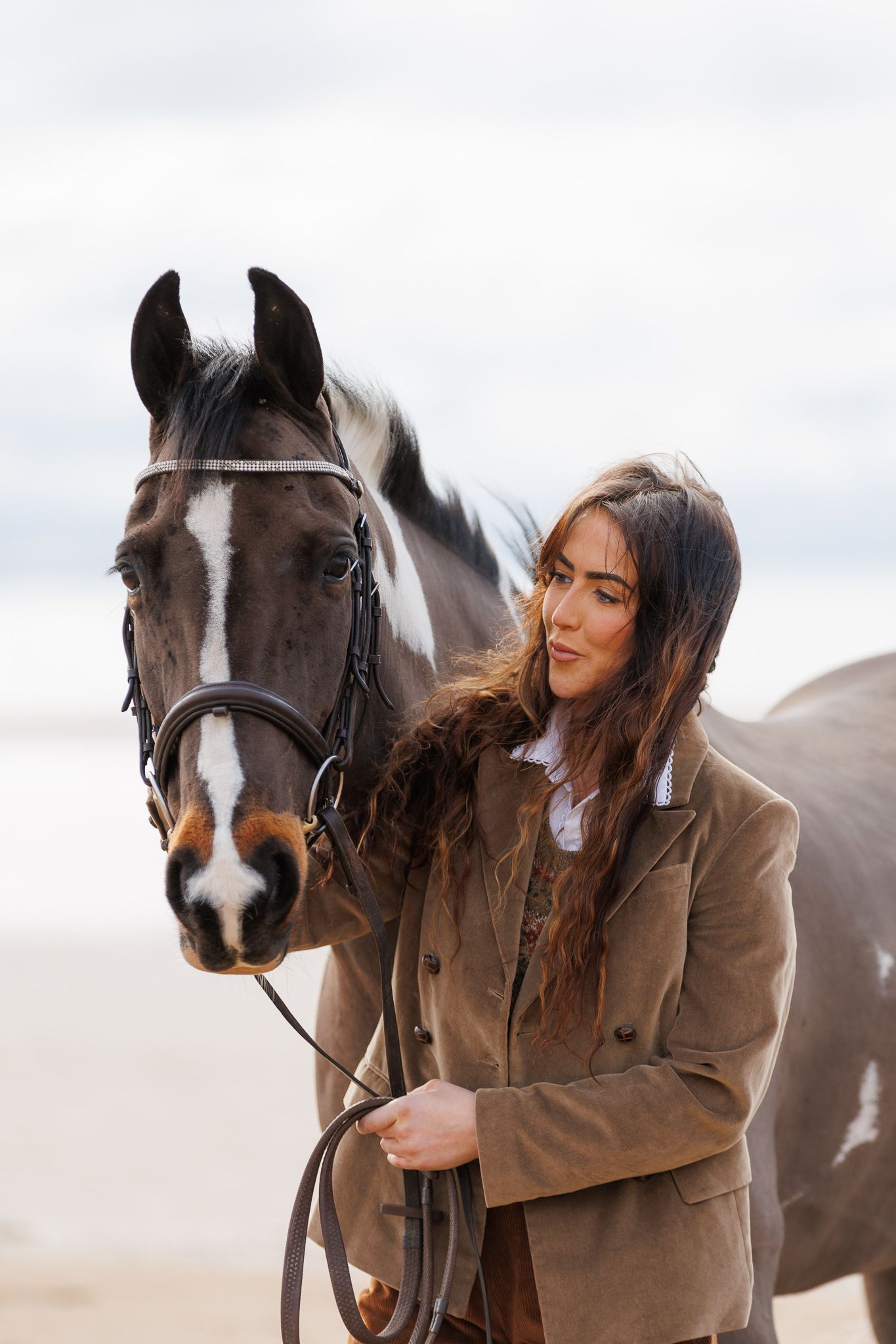 A brown horse and rider in a white sweater pose together against autumn foliage in soft natural lighting.