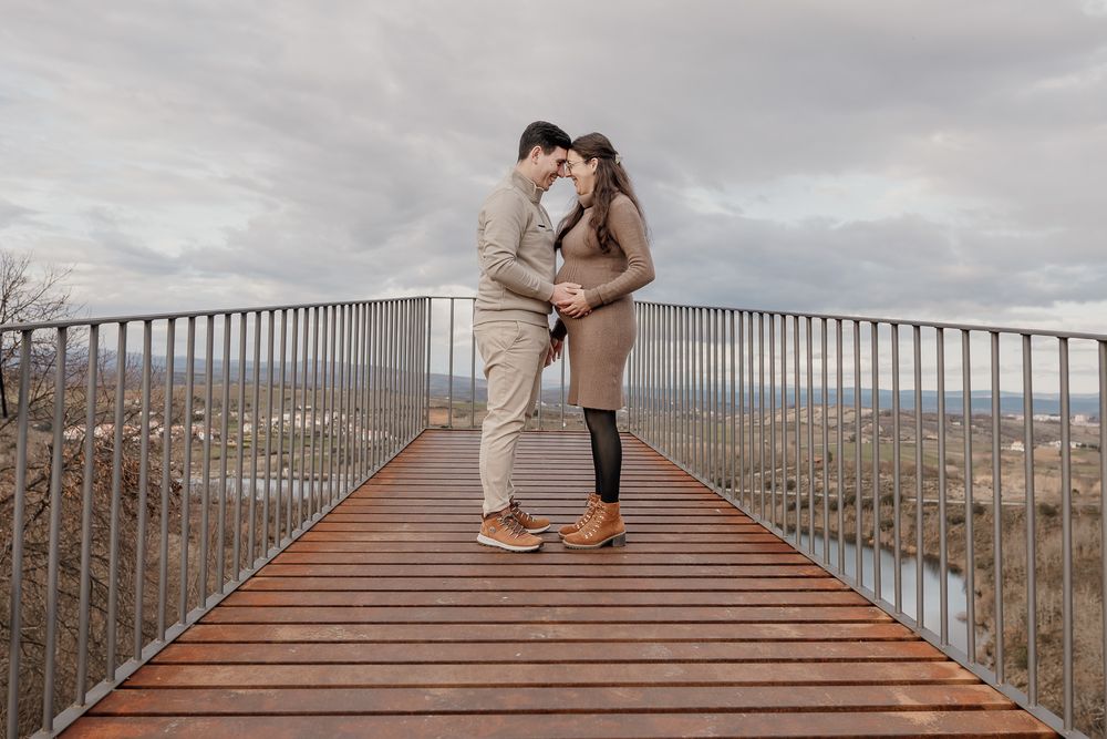 A couple shares a romantic moment on a wooden footbridge overlooking a scenic mountain landscape.