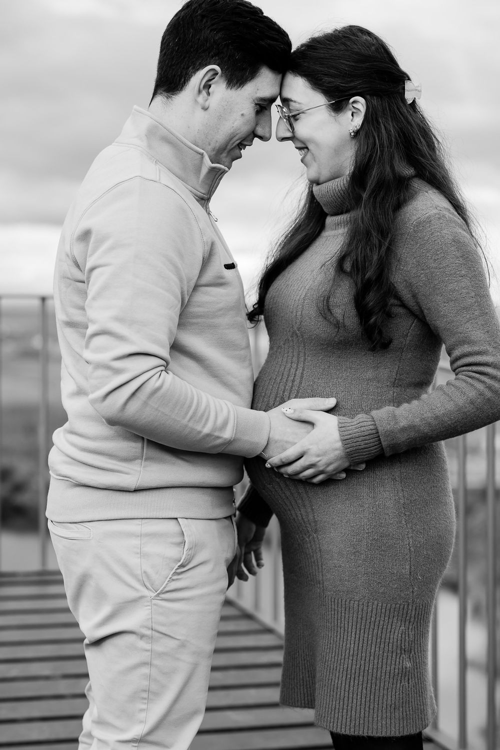 A couple in monochrome share an intimate moment as they embrace, with the person in gray touching a pregnant belly.