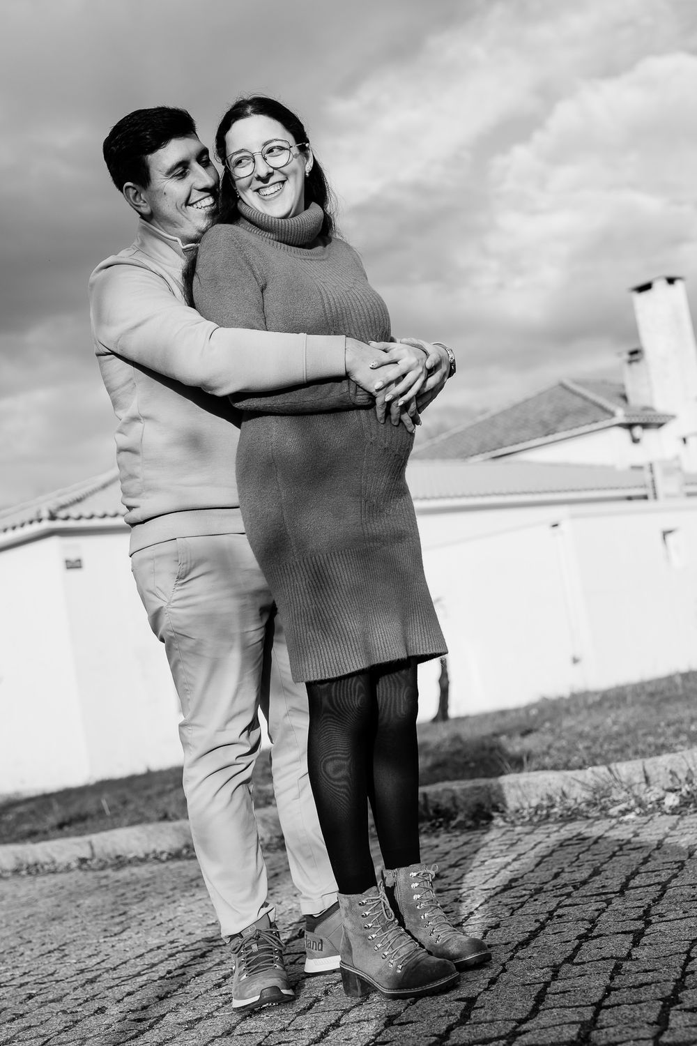 A sequence of black and white photos showing two people embracing outdoors against a cloudy sky and stone path.