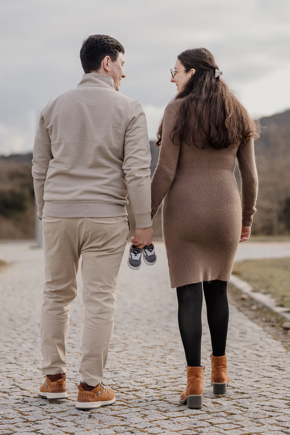 Couple wearing matching brown and beige outfits walking together on cobblestone path shown from behind in progression.