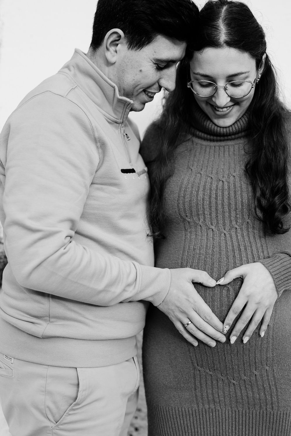 Black and white maternity photo series showing couple lovingly touching pregnant belly in matching sweaters.