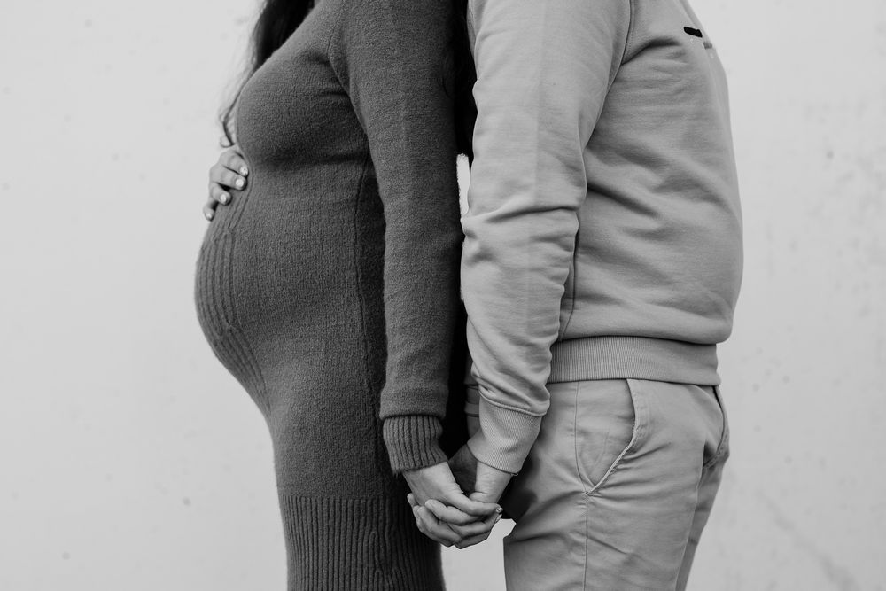 Black and white photo showing a pregnant woman in a sweater holding hands with someone in casual attire.