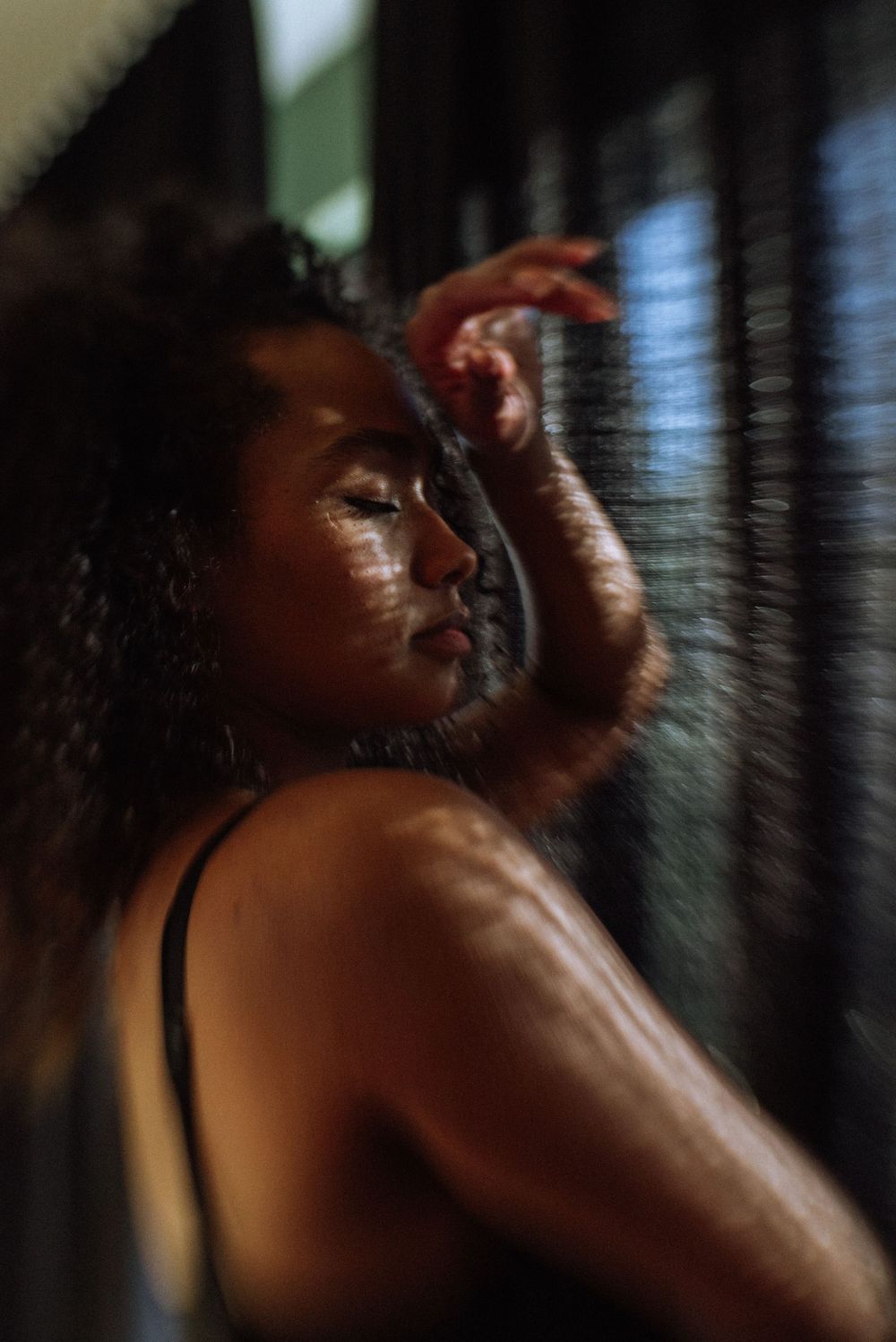 Artistic portrait with dramatic shadows from window blinds creating striped lighting effects.