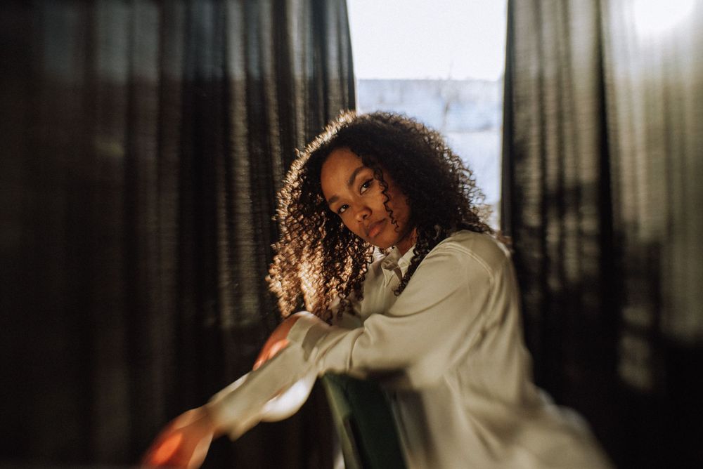 Side profile portrait with natural window light filtering through dark curtains.