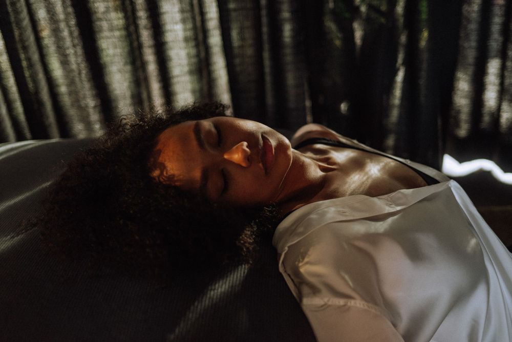 Reclining figure in white clothing with dramatic window light and shadows.