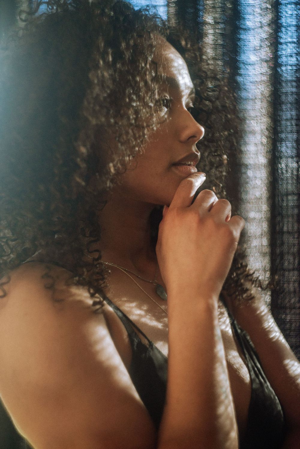 Contemplative side view portrait with natural curls in soft window lighting.