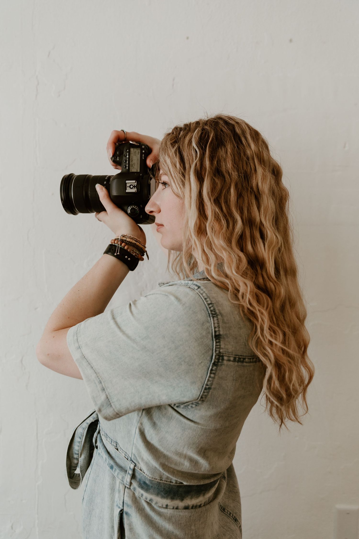 A person in a floral top and jeans sits cross-legged on a drop cloth surrounded by camera equipment and accessories.