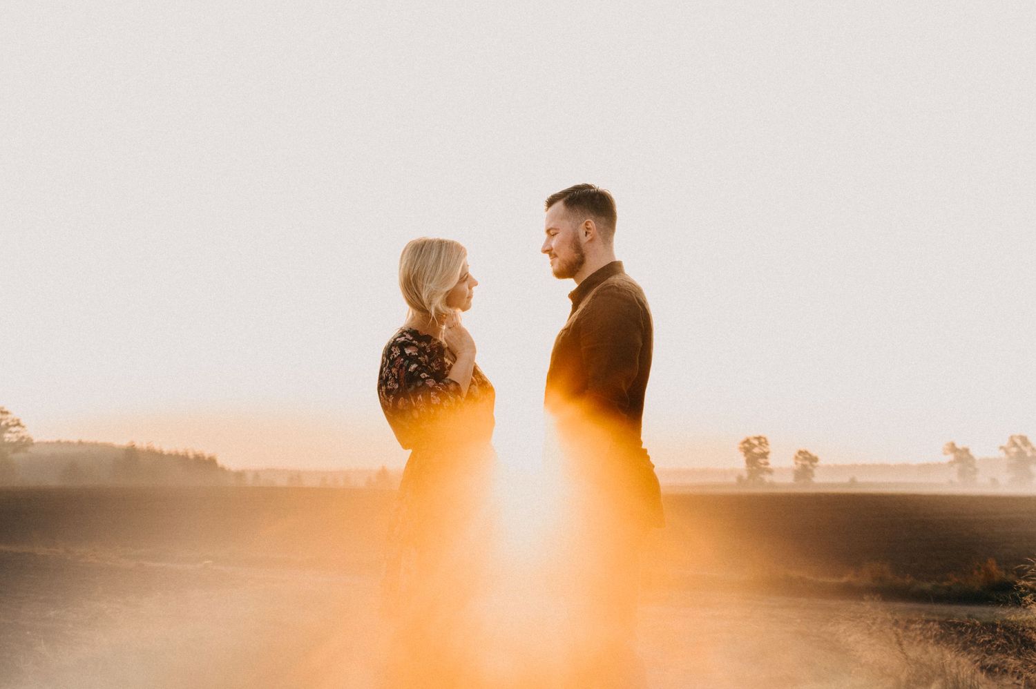 Couple embracing during golden hour sunset against a bright sky.