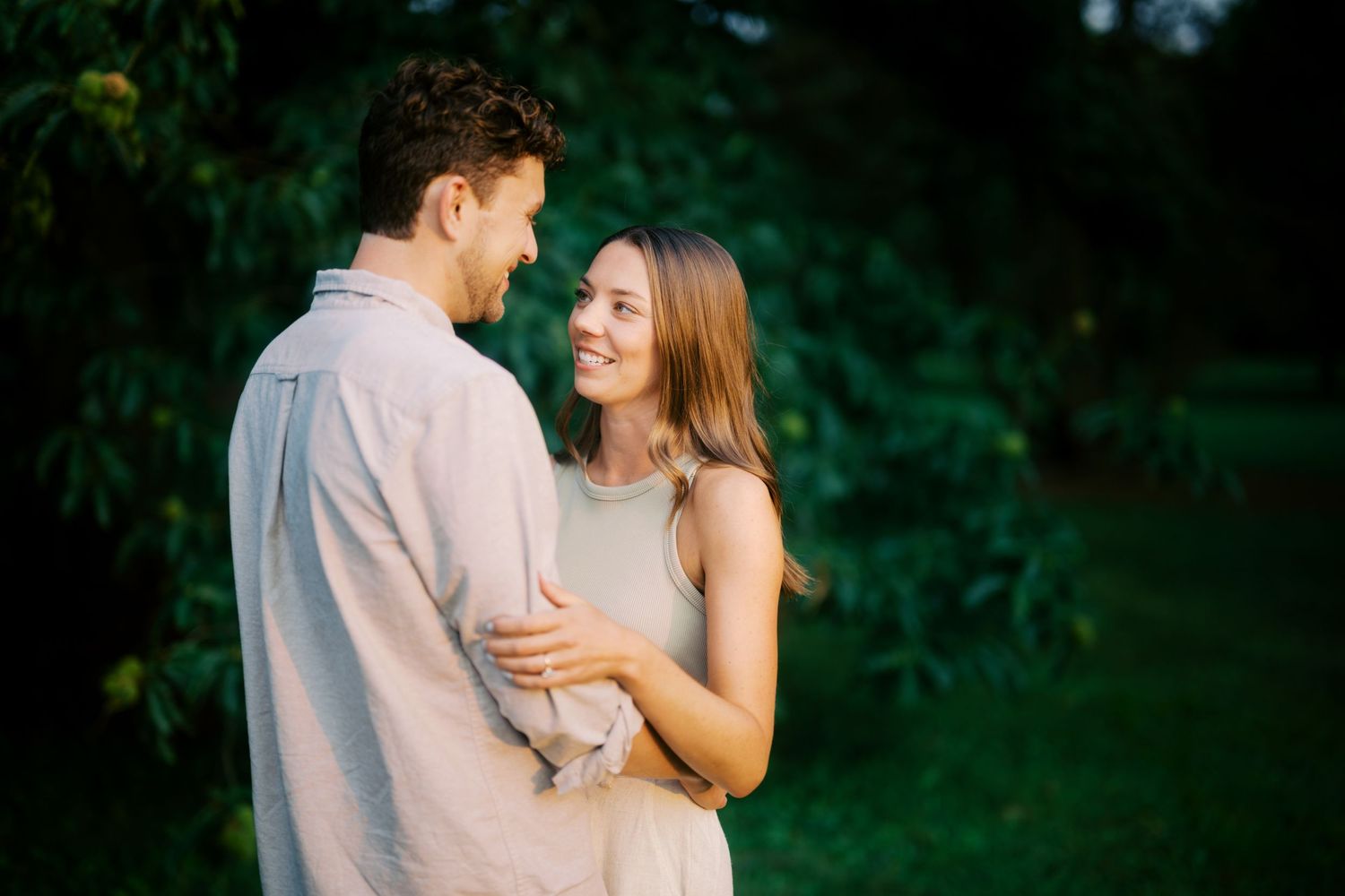 A romantic couple embraces while sharing an intimate moment against a lush green background in soft lighting.