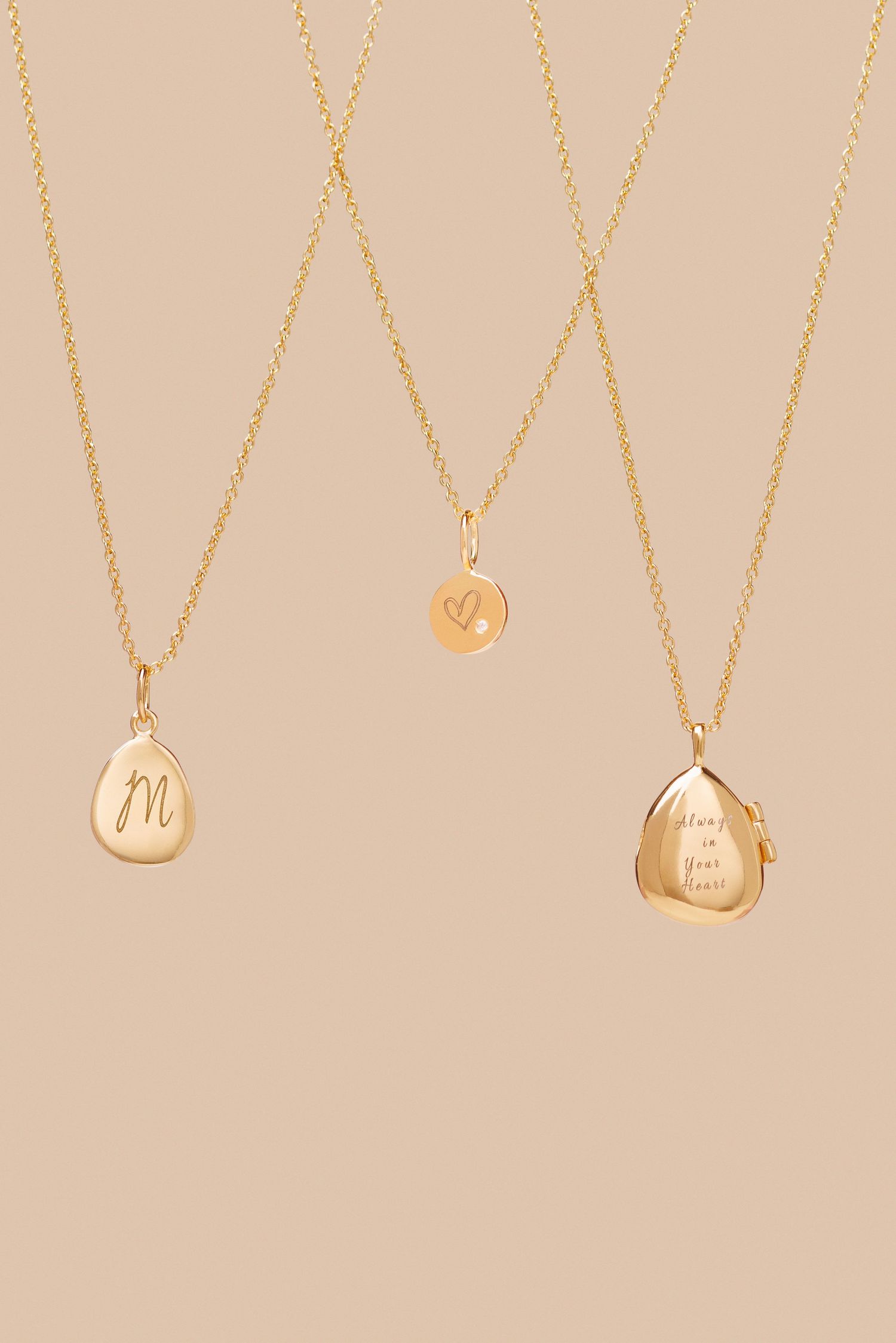 Three delicate gold necklaces with pendant charms displayed on beige background.