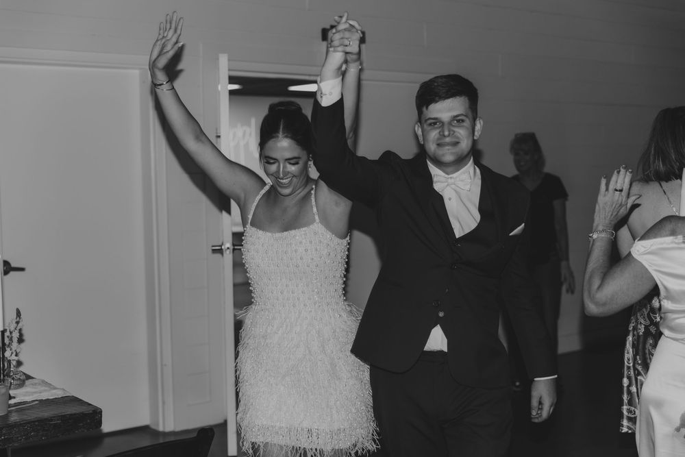 Black and white photo of a couple dancing joyfully at a wedding reception, bride in fringed dress, groom in tuxedo.