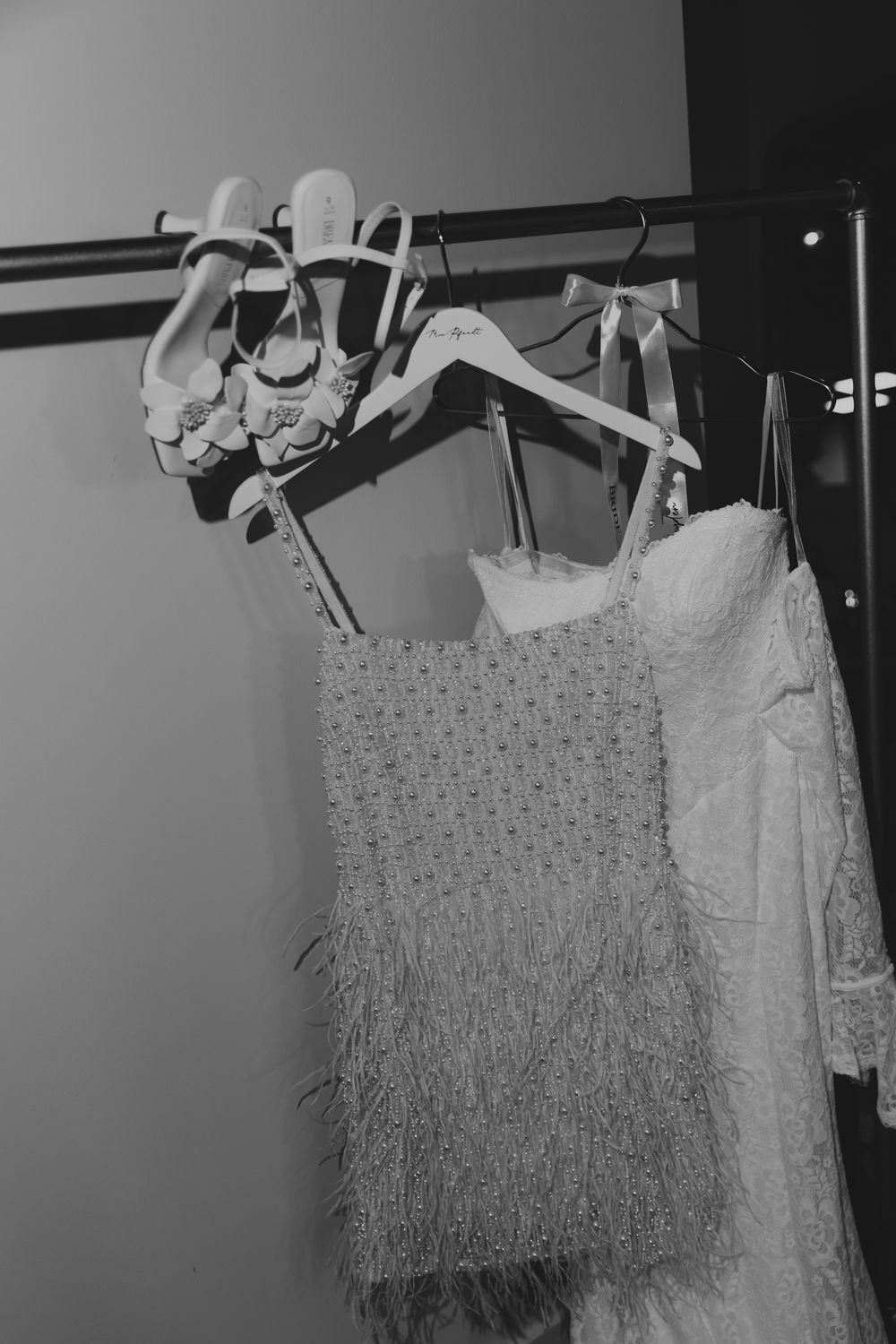 Black and white photo of elegant dresses and heels hanging on a clothing rack.