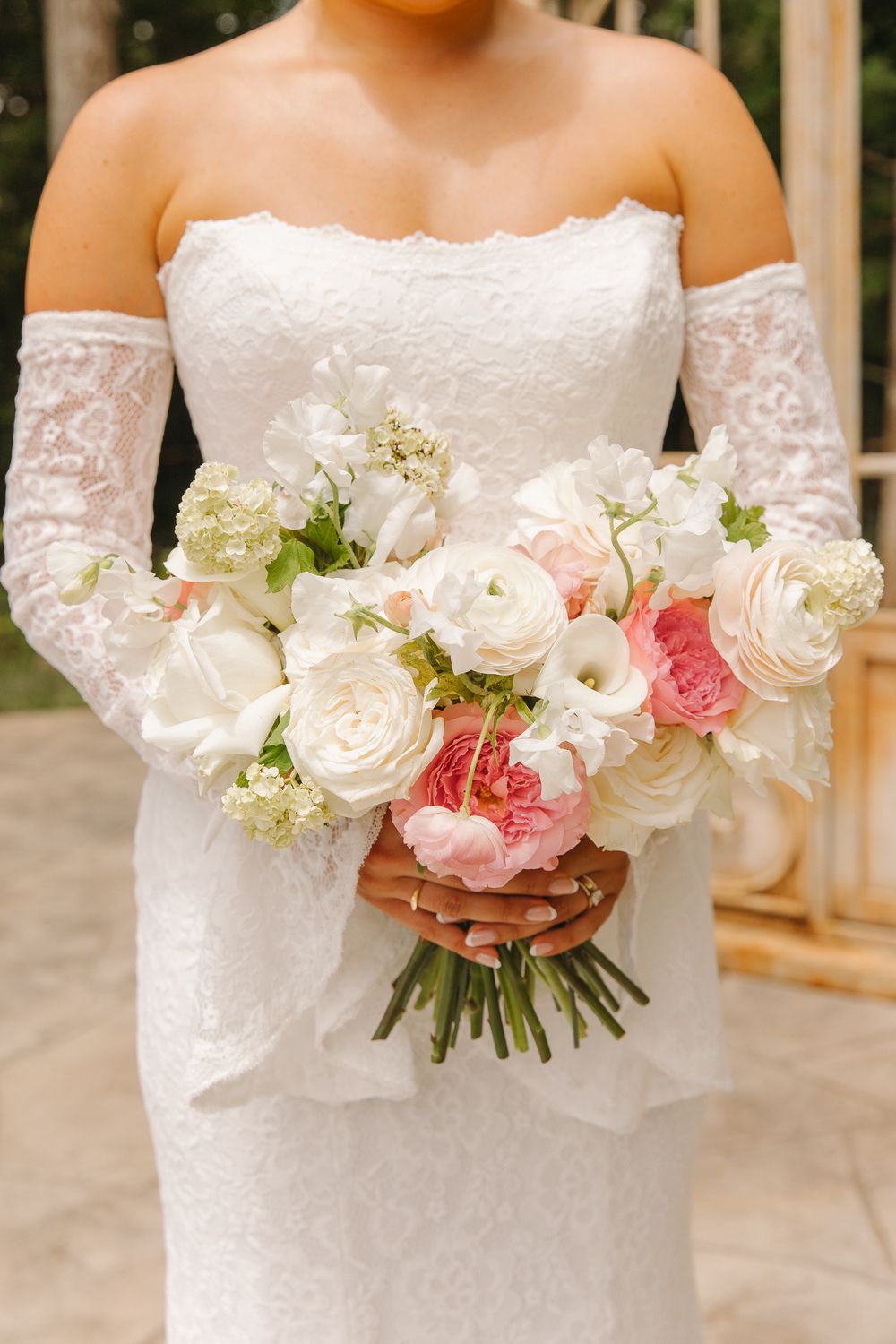 Bride in white lace strapless gown and gloves holding a bridal bouquet of pink and white roses and ranunculus.
